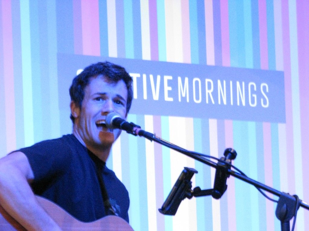 Guitarist singing in front of a striped Creative Mornings backdrop