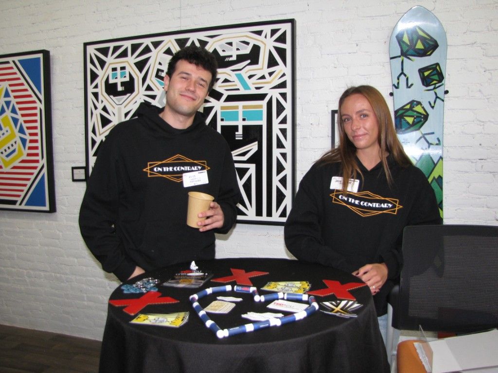 Two TEDx CU volunteers in On the Contrary hoodies behind a sticker table