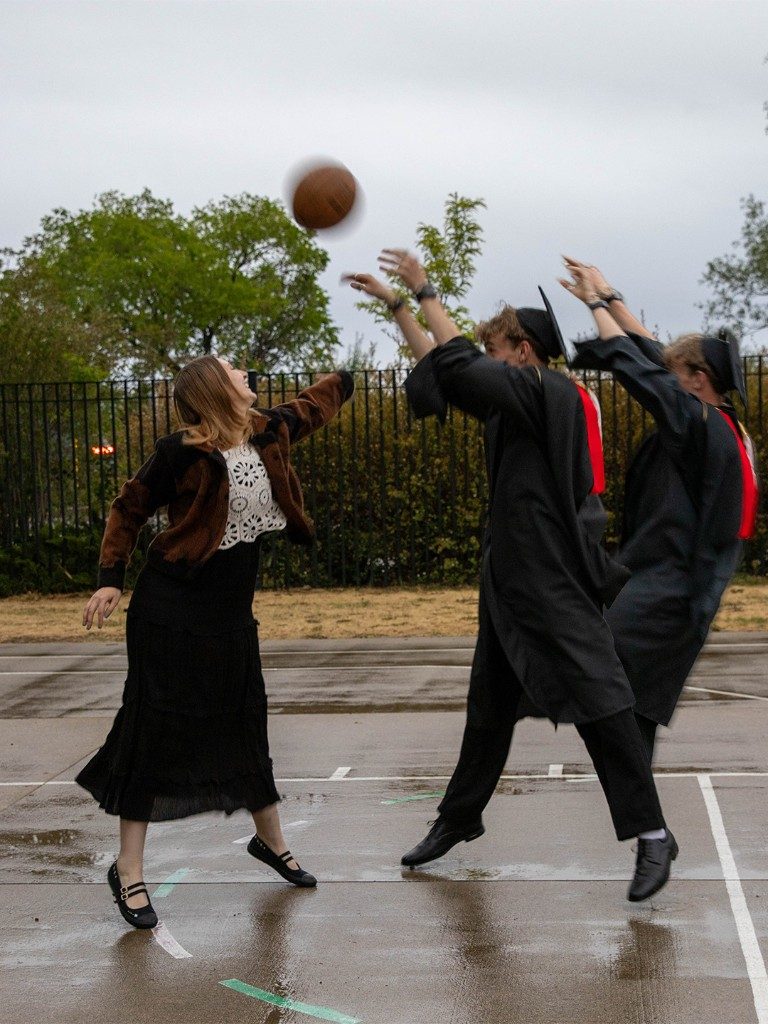 Two graduates jumping for a basketball with a friend