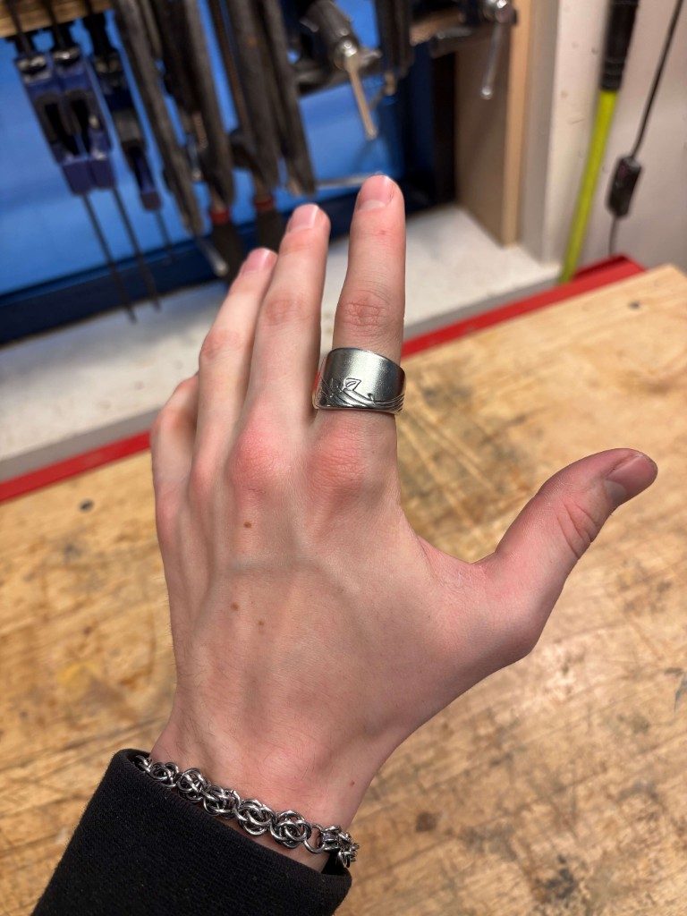 Silver spoon ring on index finger with workshop clamps behind