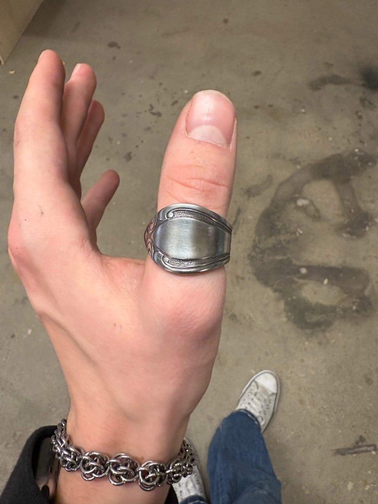 Smooth-face silver spoon ring on thumb over concrete floor