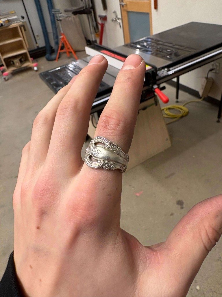Ornate silver spoon ring on index finger in workshop
