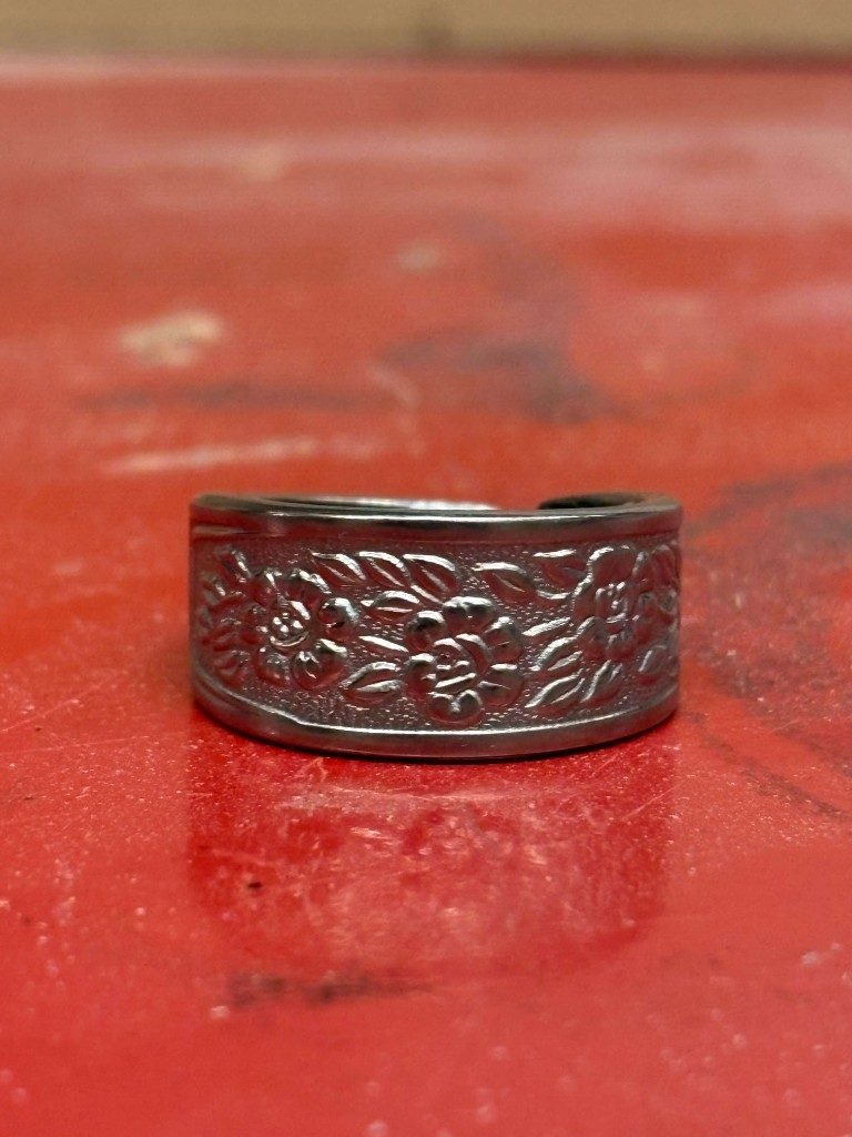 Wide rose-pattern silver spoon ring on red surface