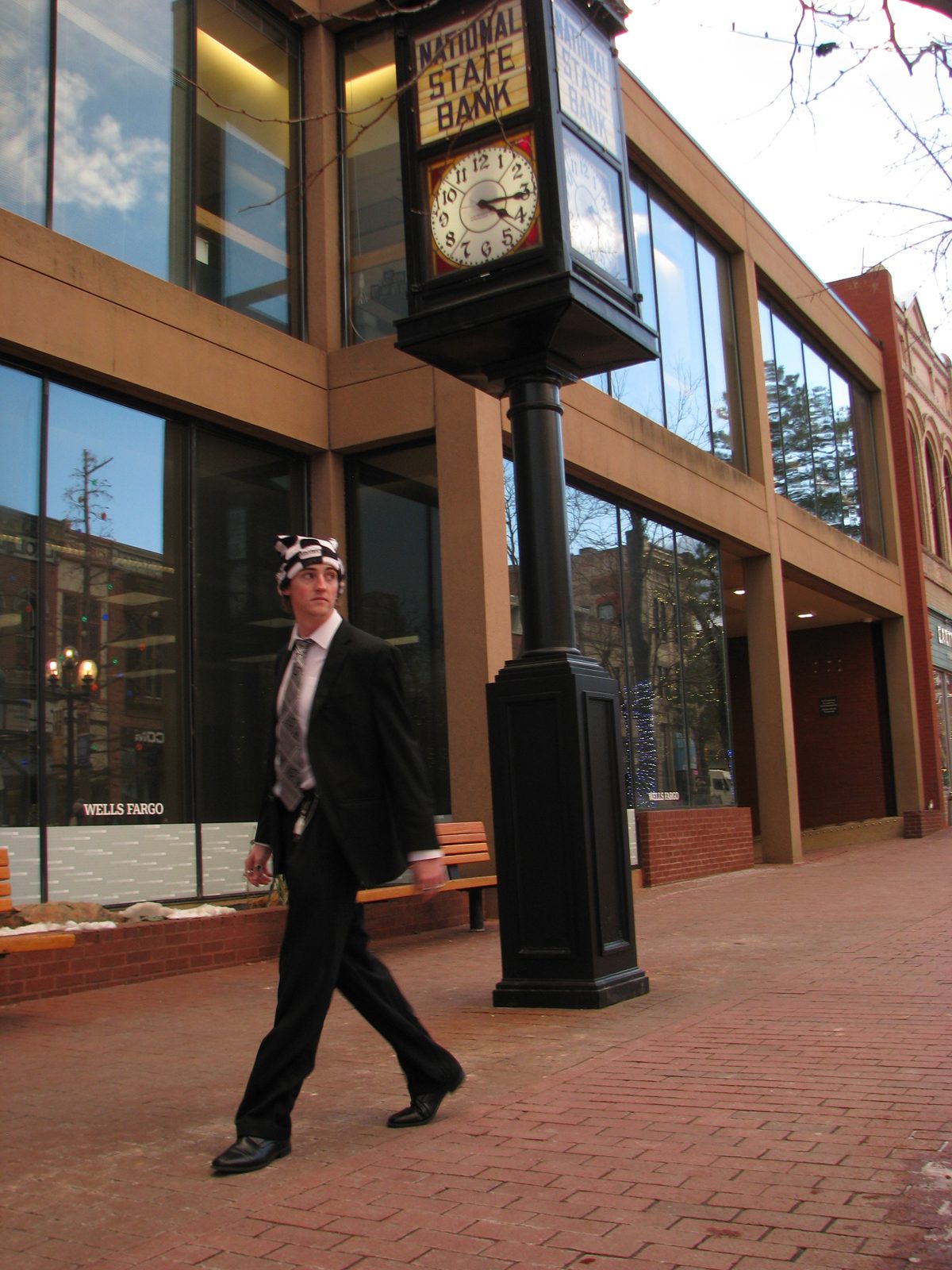 Person in a suit walking past a street clock wearing a Node star