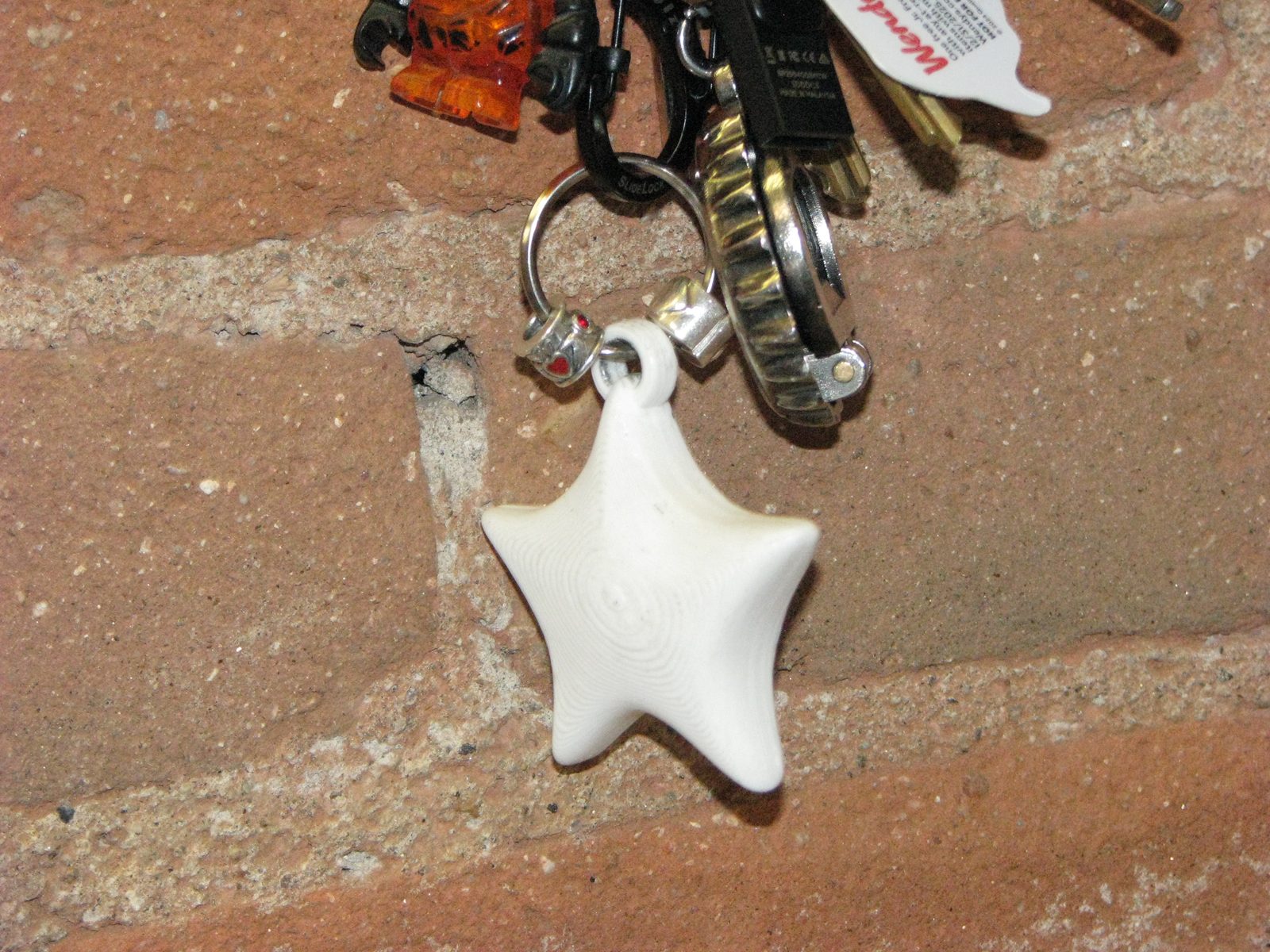3D-printed white star charm on a keychain against brick