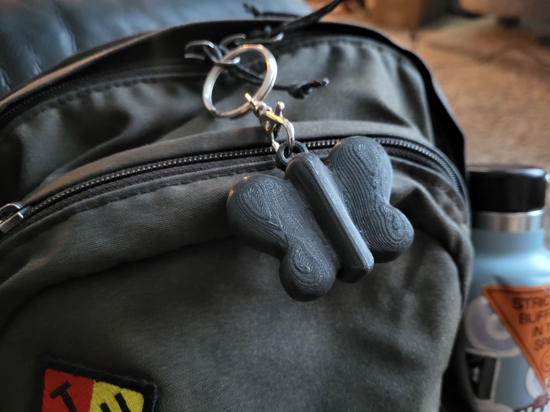 Grey 3D-printed butterfly NODE charm clipped to a backpack