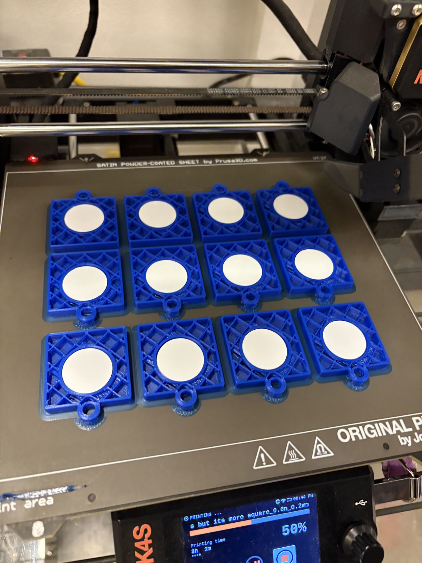 Blue square NODE charms printing on a 3D printer bed