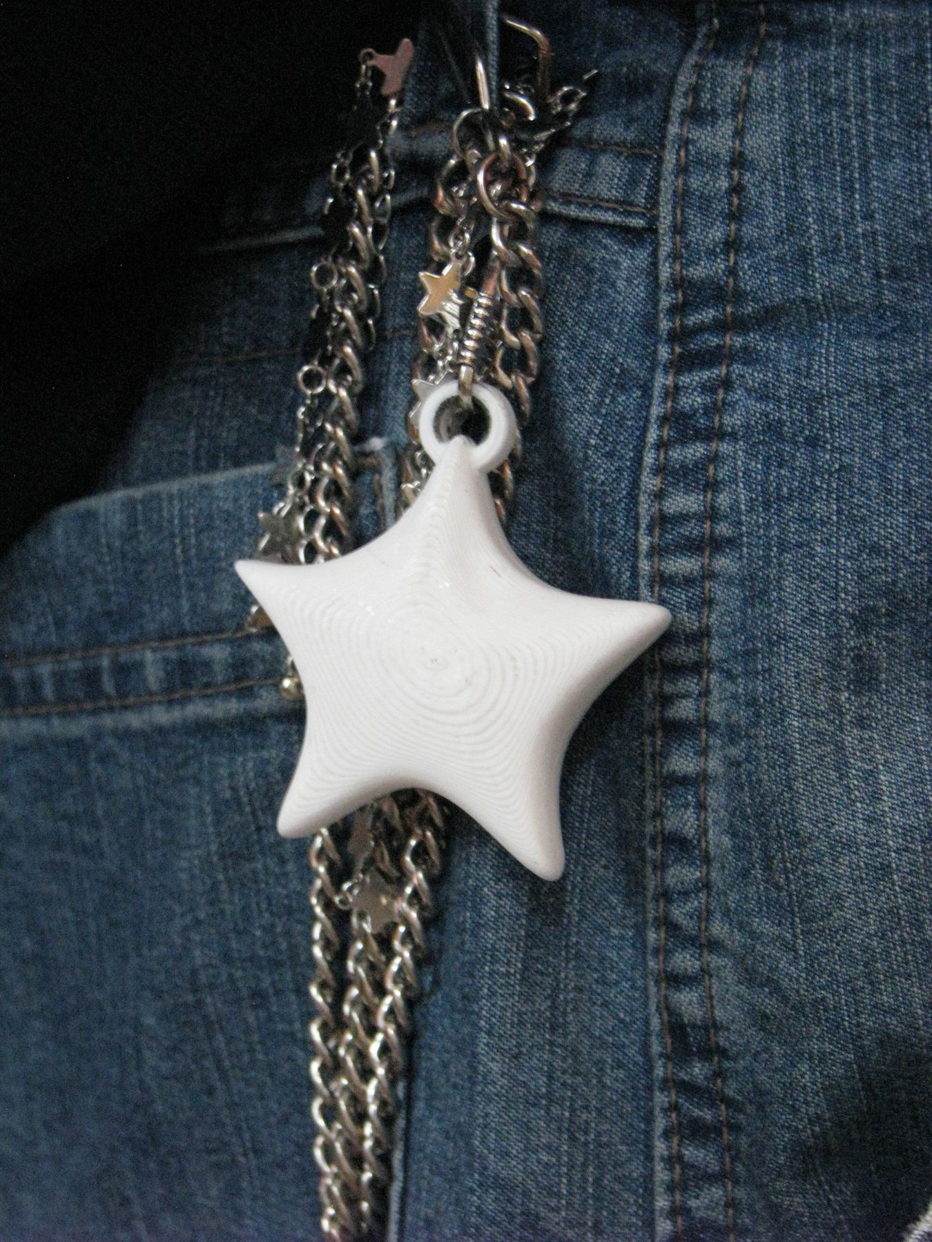 Close-up of the white star NODE charm hanging from jean chains