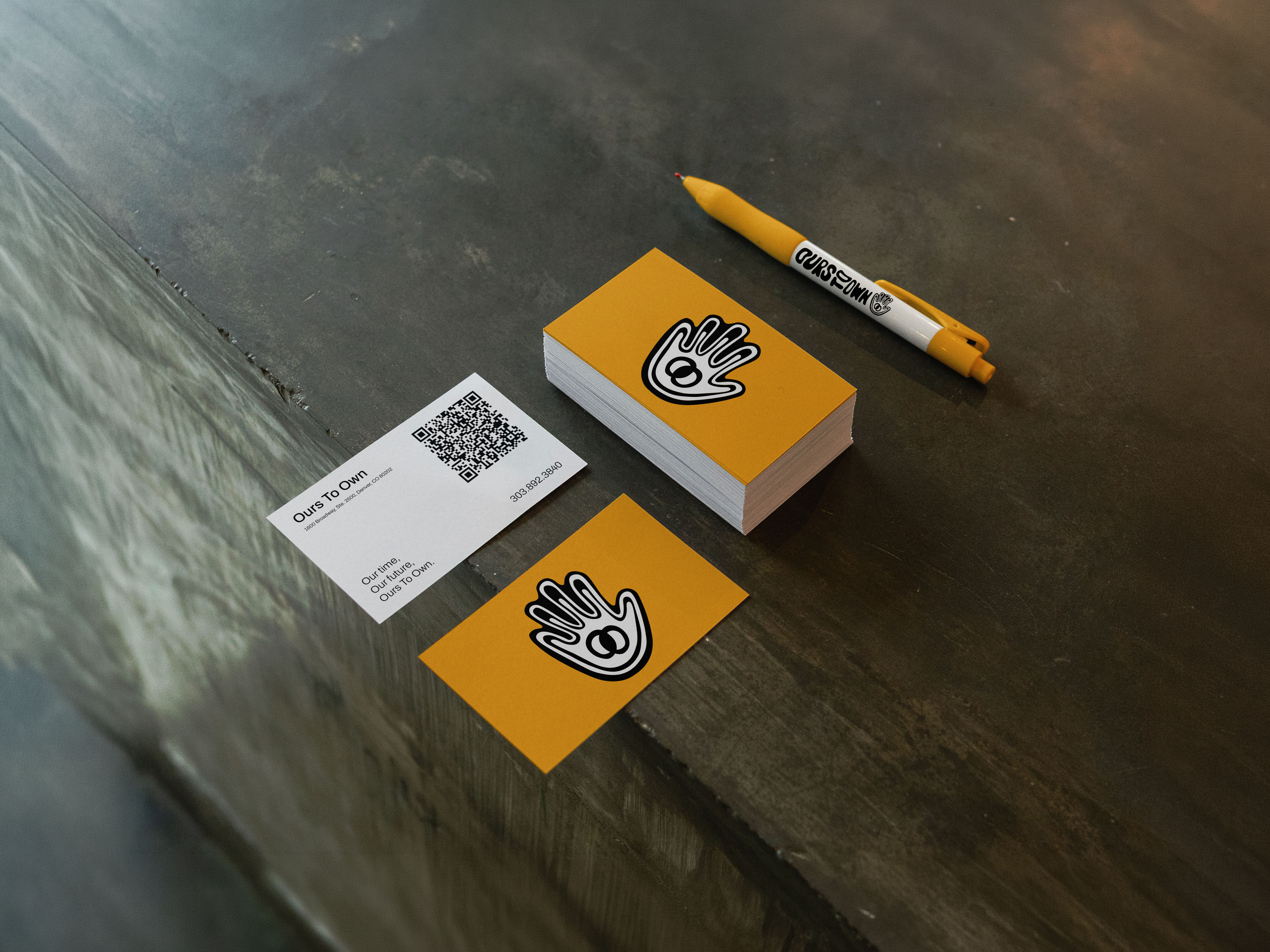 Ours To Own business cards and branded pen on a dark surface