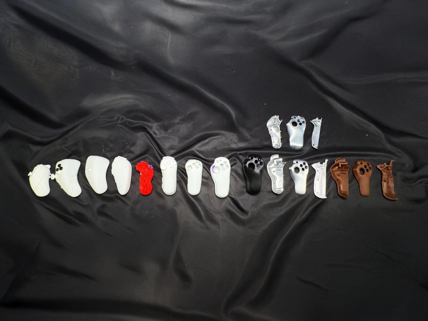 Line of 3D-printed SPUD controller iterations on black fabric, from early forms to later refined shells