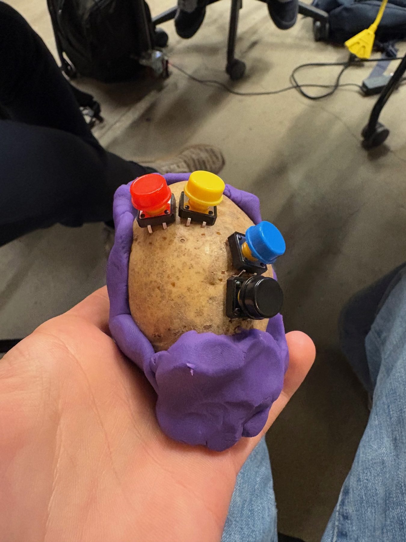 Hand holding an early potato controller prototype with purple Play-Doh grip and colored buttons
